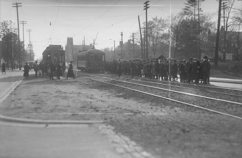 Two streetcars sit side by side on the tracks. A line of people is leaving one and lining up to board the other.