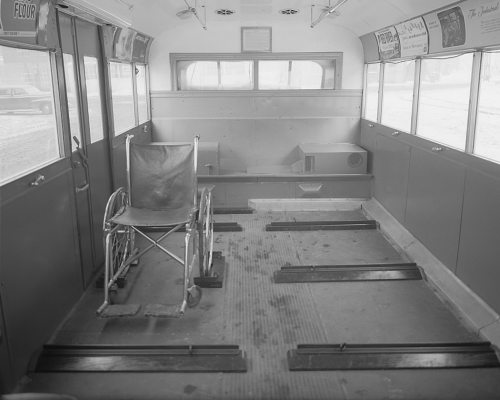 The interior of a bus. Seats have been taken out and replaced with flat spaces and bumpers. An empty wheelchair is sitting in one of the spaces.