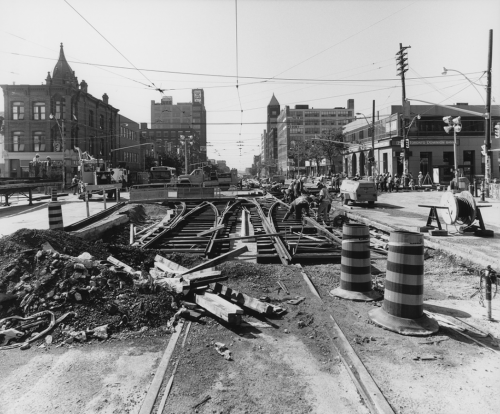 Laying new track and special trackwork along intersection. Background shows storefronts.