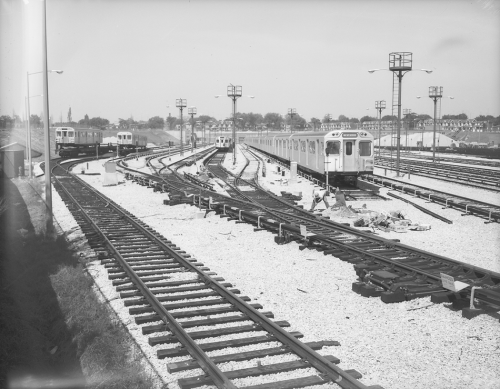 Subway cars on track in yard and other subway cars on flatbeds.