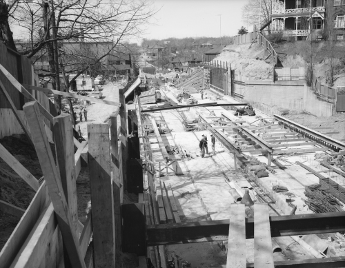 Installation of subway track on newly formed subway trackbed. Hoarding runs along either side of structure.