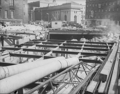 Beams laying over excavated area. Union Station and other buildings in background.