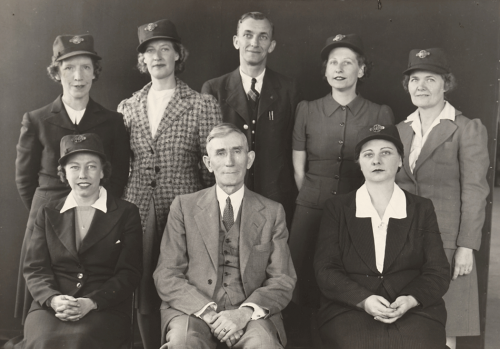 One man and two women seated with one man and four women standing behind. All of the women are wearing hats with TTC badges.