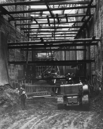 Heavy machinery and construction workers underground with hoarding and horizontal beams installed in tunnel