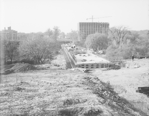 Nearing completion of installation of subway trackbed on bridge. Background shows trees and erection of structure for tall building.