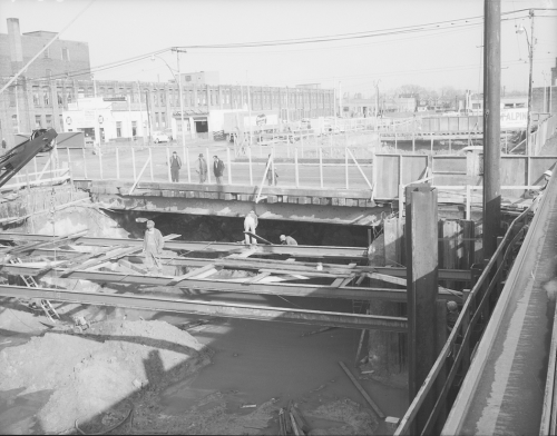 Workers installing of beams for mezzanine roof. Men are looking through chain-link fence at workers.