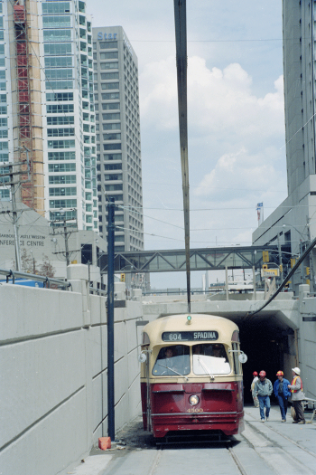 PCC streetcar emerging from tunnel with four construction men alongside checking its clearance.