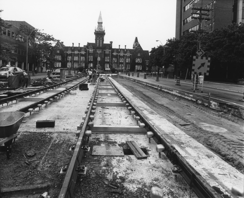 Newly installed streetcar tracks on right of way. Background shows the building at 1 Spadina Crescent.