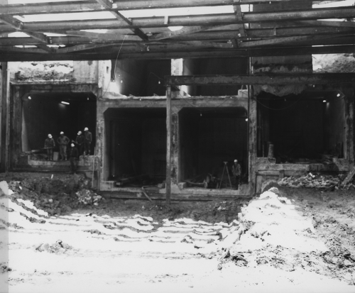 Six square tunnel structures. Four lower with group of workers standing in one and surveyor with equipment located in another.