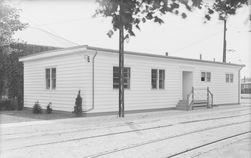 Perspective view of white one storey building near streetcar tracks.