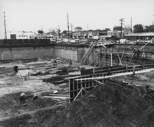 Works in excavated pit for station construction. Background shows storefronts.