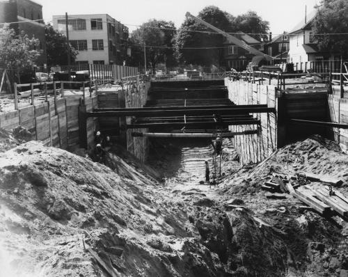 Cross section of excavated area and horizontal beams in place with houses and small buildings at street level