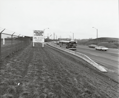 Construction sign "a public transit project Spadina Subway Extension to Sheppard Avenue" on grassy area busy busy roadway.