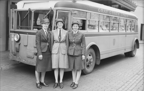 Three women in uniform standing near bus.