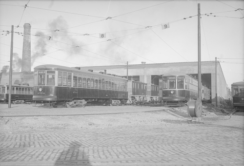 A row of streetcars on tracks outside the open doors of a one-storey garage.