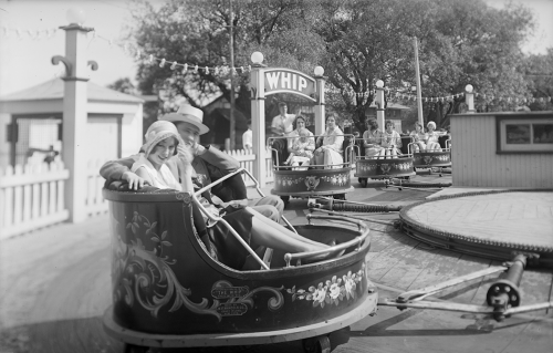 Two people are sitting in a round open cup with flowers painted on the outside. Behind them are visible more identical cups that are moving around in a circle.