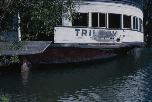 An old wooden ferry with its red and white paint fading is sitting in the water.