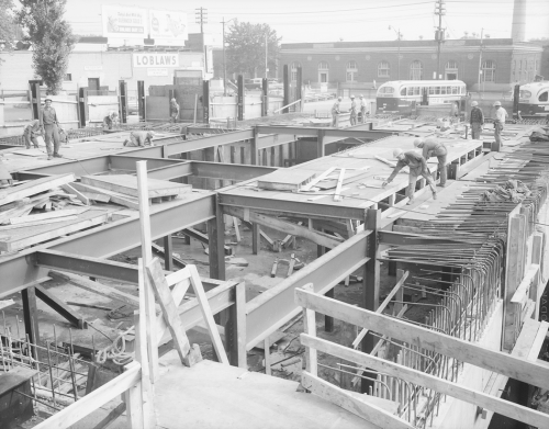 Street level with workers standing on partially installed mezzanine roof with PCC is background and one storey brick building