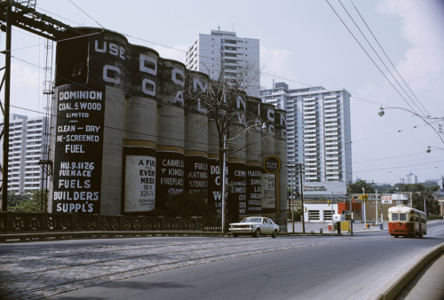 A red and cream coloured streetcar drives past large concrete silos painted with the words "Use Dominion Coal."