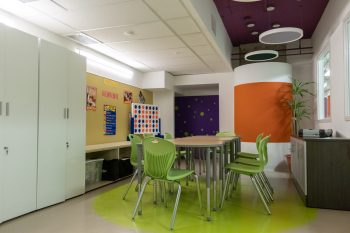 Table with green chairs and bright orange walls. 