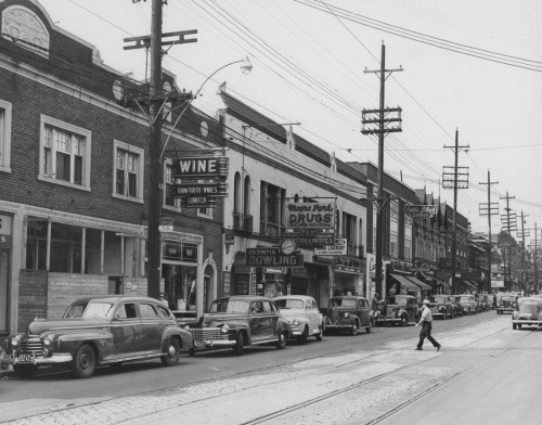 A row of brick stores and services, including Danforth Wines, Olympia Bowling, Moore Park Drugs, and Eddie Black Radio.