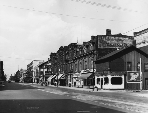 A street of three-storey brick stores, including a Dominion grocery store and the White Chef restaurant.