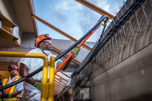 A Black man in a hardhat guides a thick cable onto hooks.