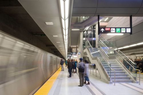 People stand on a subway platform while a train passes then in a silver blur.