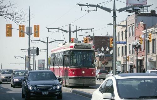 A streetcar drives down a raised concrete platform with lanes of cars on either side.