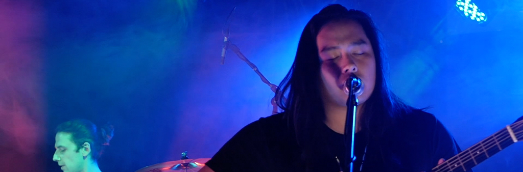 Image depicts close up shot of male musician, playing a guitar, singing into a microphone.