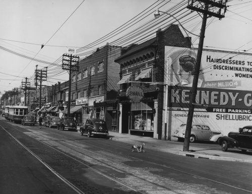 A row of brick store, the edge of a parking lot, and a billboard advertising a hairdresser.