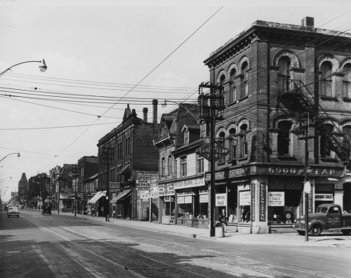 A street lined with stores, some of them made of brick, and some smaller and made of wood.