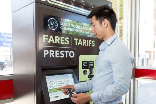 An Asian man uses a touchscreen on a ticket machine.