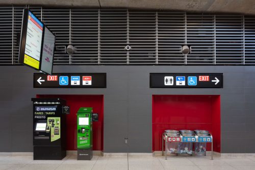 In a subway station , a digital screen and signs on the wall direct people to subway lines, elevators and exits.