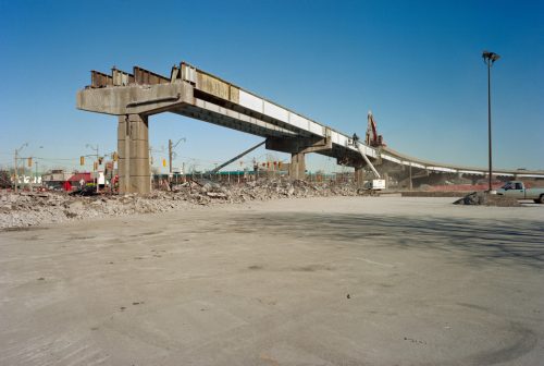 Concrete pillars supporting metal beams of a former highway that ends as if it has been cut off.