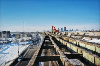 Large machine hammers away concrete on bed of raised expressway, leaving only metal support beams.