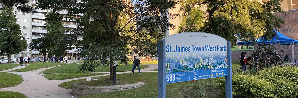 The image shows a view looking into St. James Town West Park from the west entrance on Sherbourne Street. The park's mature trees and pathways are shown.