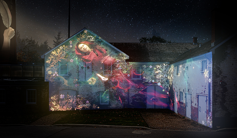 Light projections onto historic buildings of a hand holding a quill and a woman surrounded by flowers