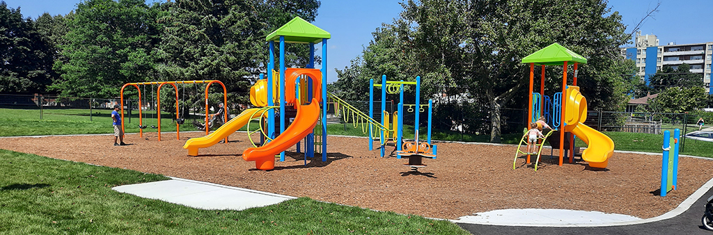An image of Dunlop Park Playground that focuses on the existing junior play structure which includes a small double straight slide, small curved slide and play panels above sand surfacing.