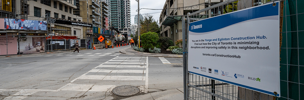Sign on construction fence telling passersby that they are in the Yonge Eglinton Construction Hub.