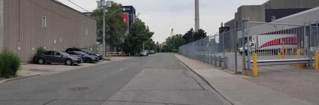 Woodfield Road flanked by UPS building to the left with parking along the building and Canada Post building and parking lot to the right.