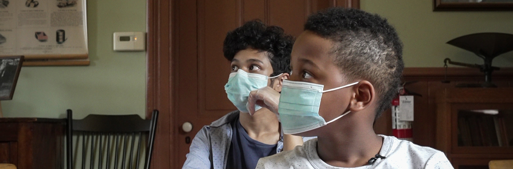 Two kids with facemasks looking sideways at something