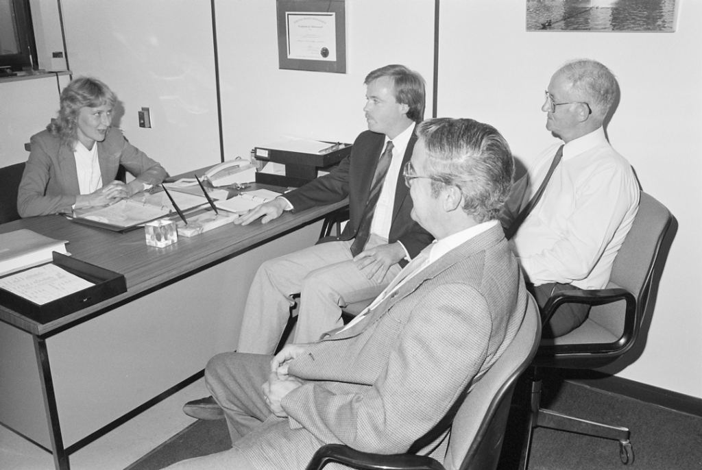 Woman behind desk speaking to three men