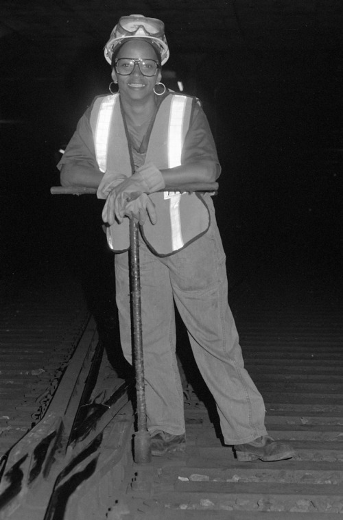 Woman in hard hat and safety vest standing in subway tunnel.