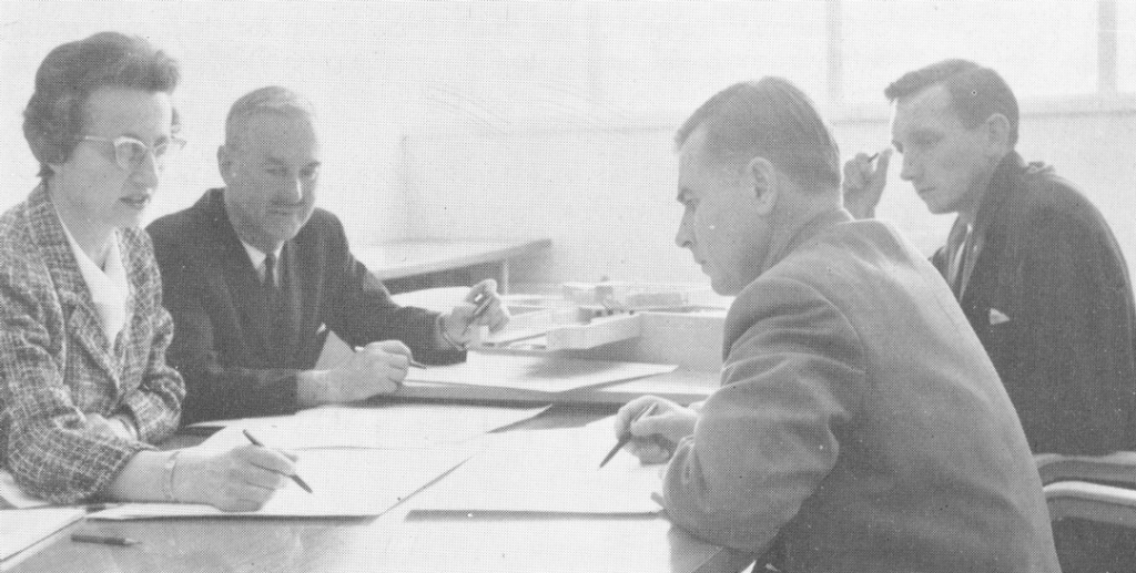 Three men and a woman sit around a table reviewing a document together.
