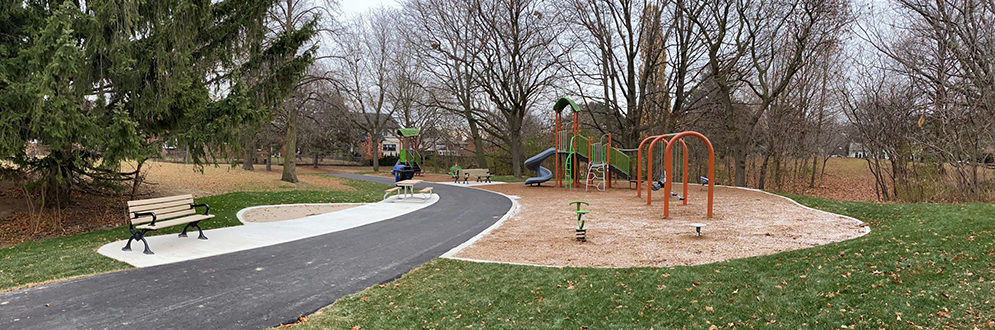 An photograph of Eden Valley Park Playground which includes a medium sized slide, swing set and spring toys on top of sand and grass.