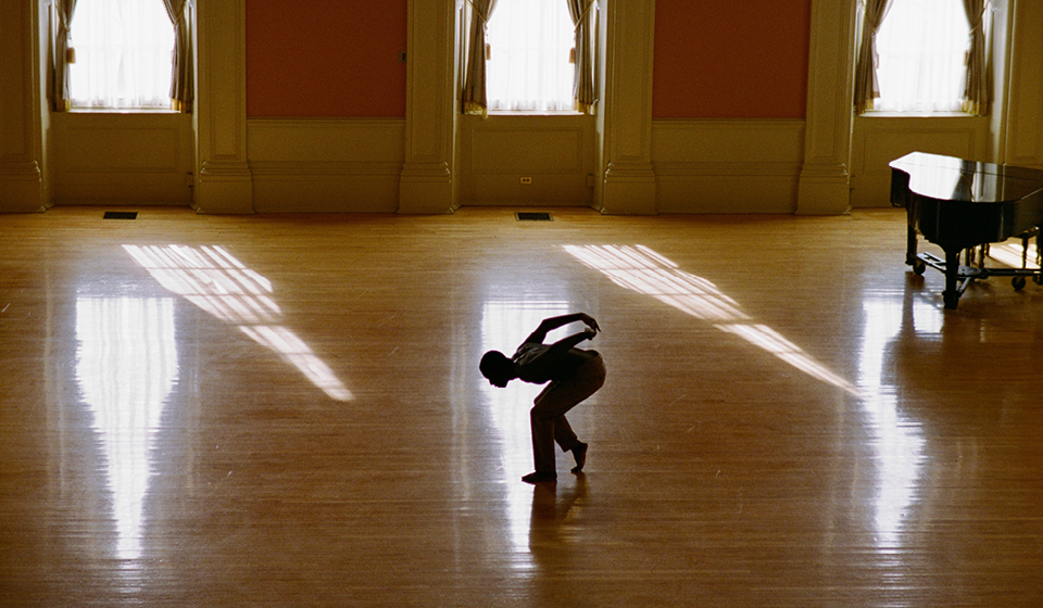 Person dancing in a sunlit gymnasium.
