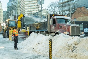large snow blower moves snow into dump truck.