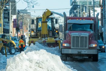 large snow blower moves snow into dump truck.