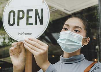 Young woman places an open for business sign in a shop window